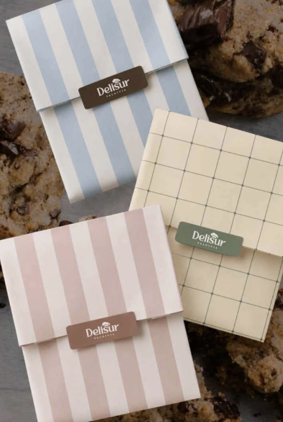 Tres empaques de Delisur a rayas celestes y rosadas junto a galletas sobre una mesa