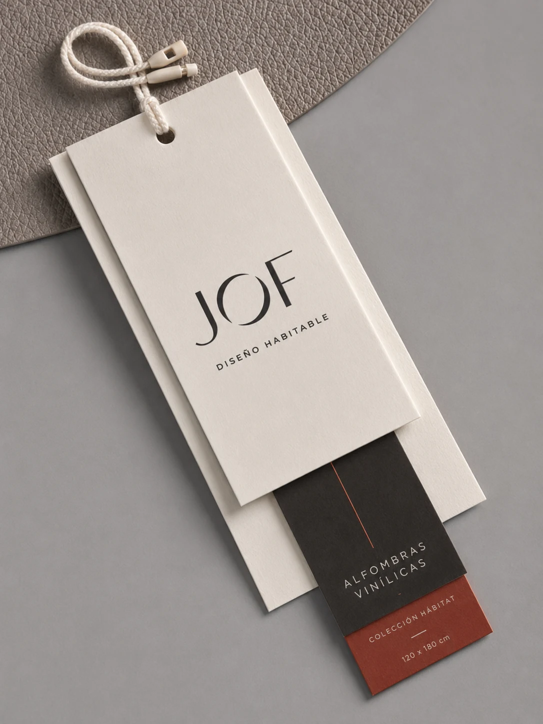 Etiquetas colgantes de JOF en color crudo y vinotinto, sobre una alfombra gris