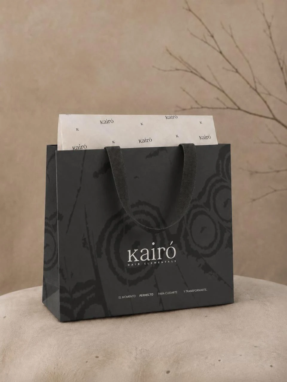 Bolsa de papel negra con el patrón y el logotipo de Kairó, sobre una base de piedra