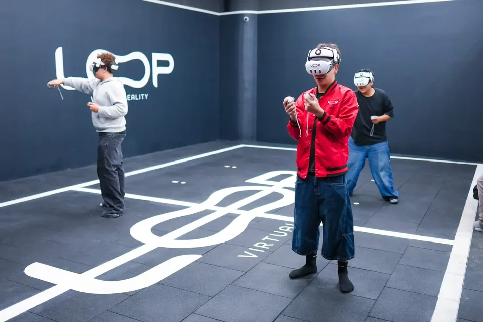 Tres personas con gafas de realidad virtual jugando en la sala de Loop, con el logotipo pintado en la pared
