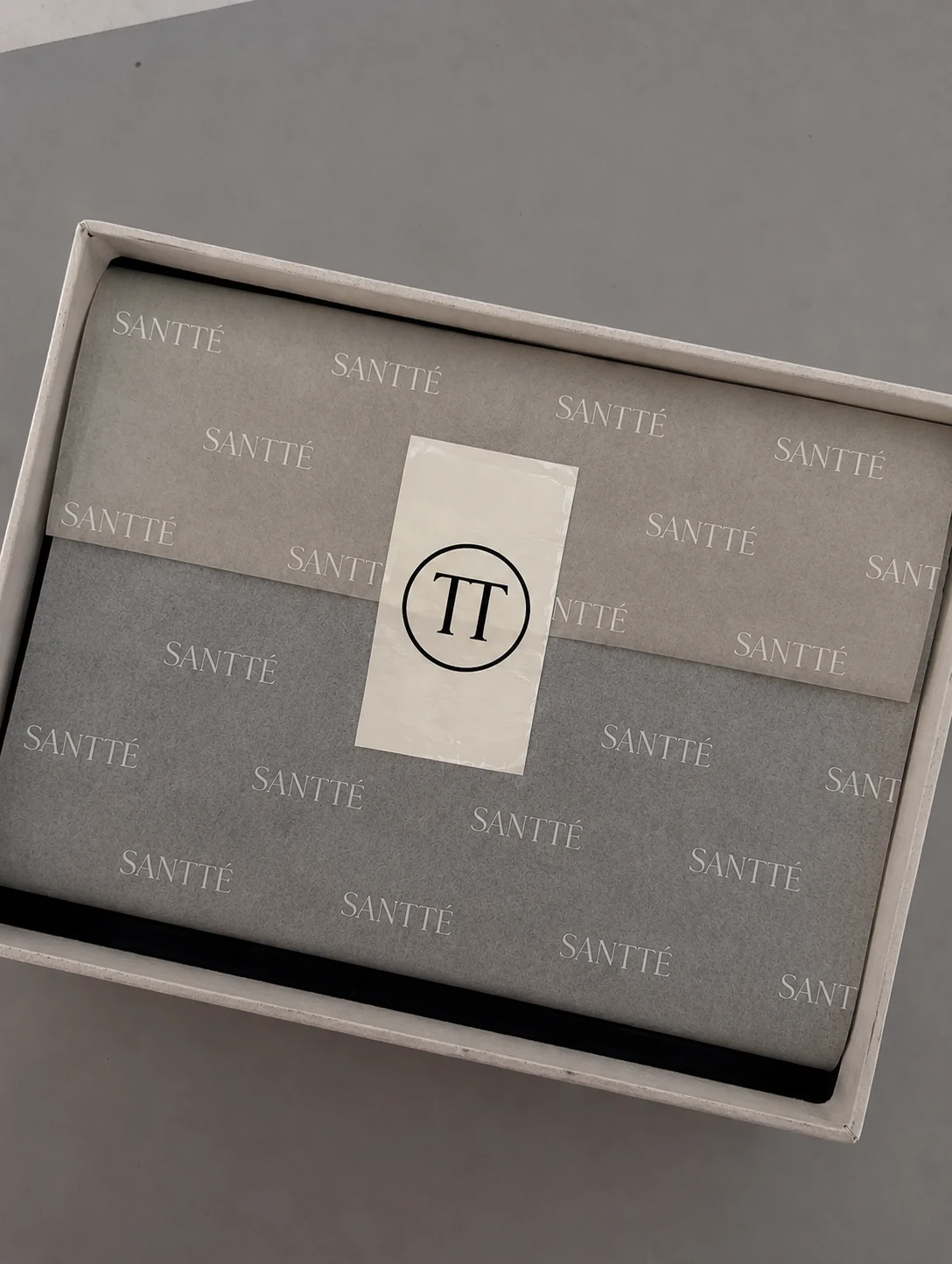 Caja de regalo gris con papel de seda estampado con el logotipo y una etiqueta con el monograma