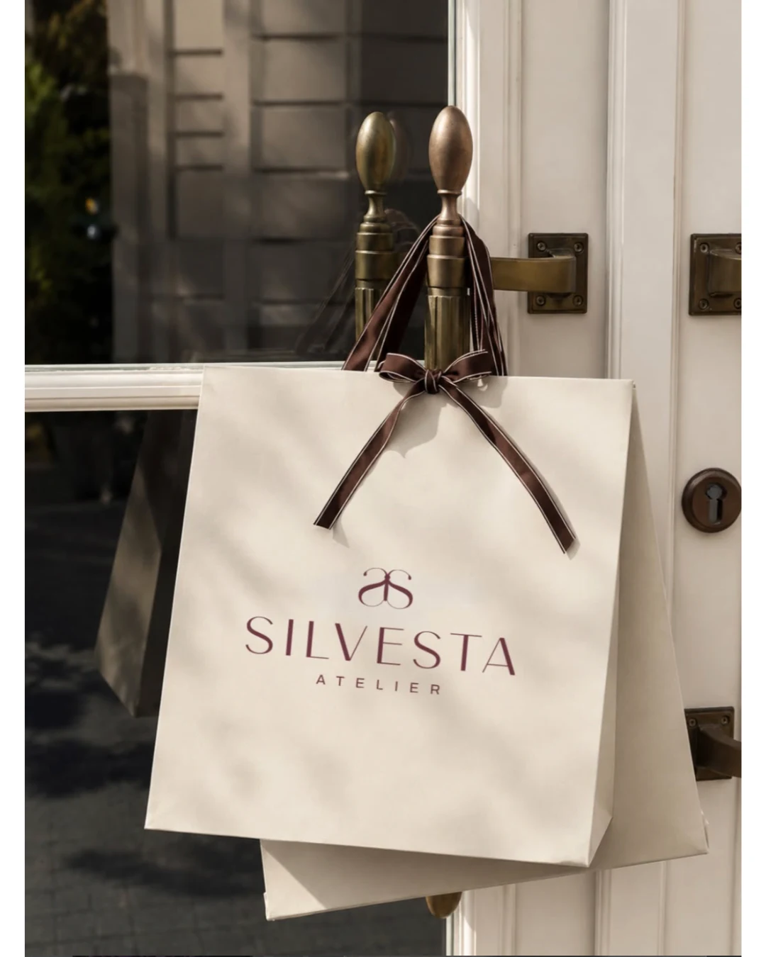 Bolsa de papel color crudo con el logotipo de Silvesta Atelier, colgada de la manilla de una puerta