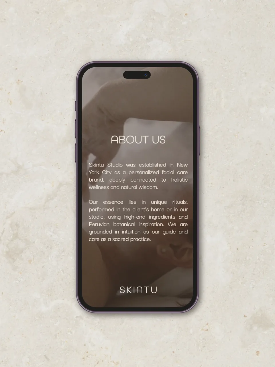 Teléfono con la sección About Us del sitio de Skintu, sobre una superficie de piedra beige
