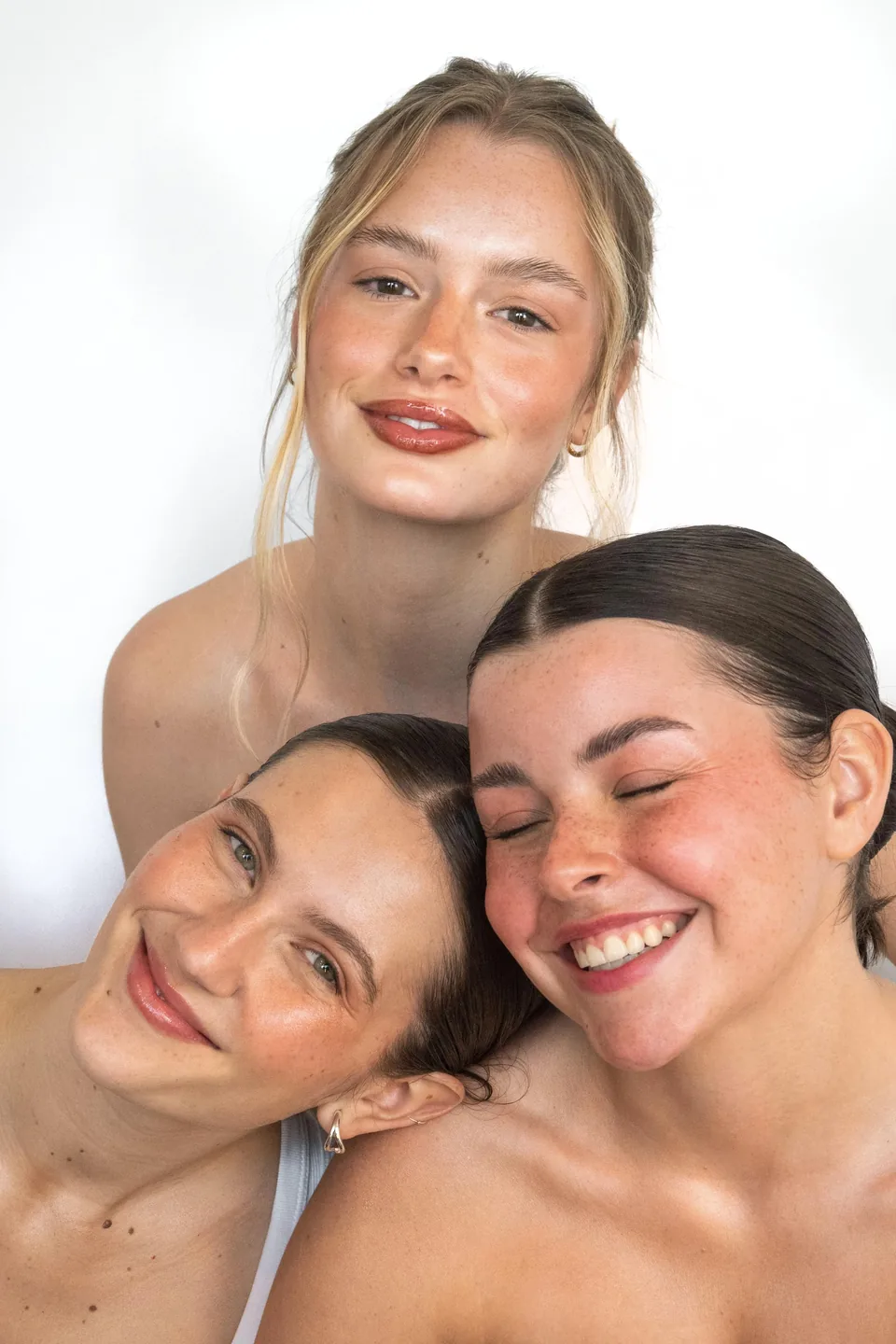 Tres mujeres juntas y sonriendo, maquilladas con la línea de Veus